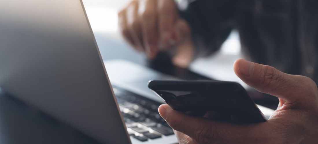 Person using mobile phone while sat in front of a laptop